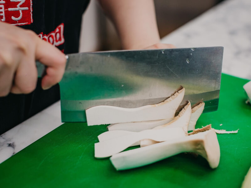 A person slicing Japanese matsutake mushrooms on a green cutting board